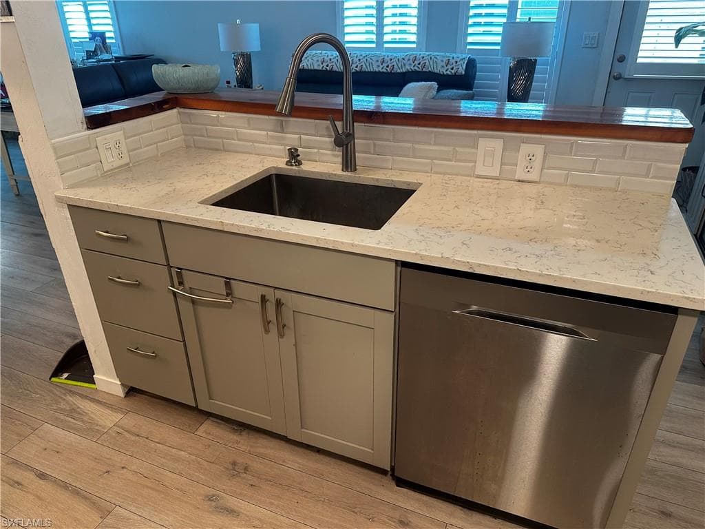 Kitchen with stainless steel dishwasher, gray cabinets, light stone counters, light wood-style flooring, and tasteful backsplash
