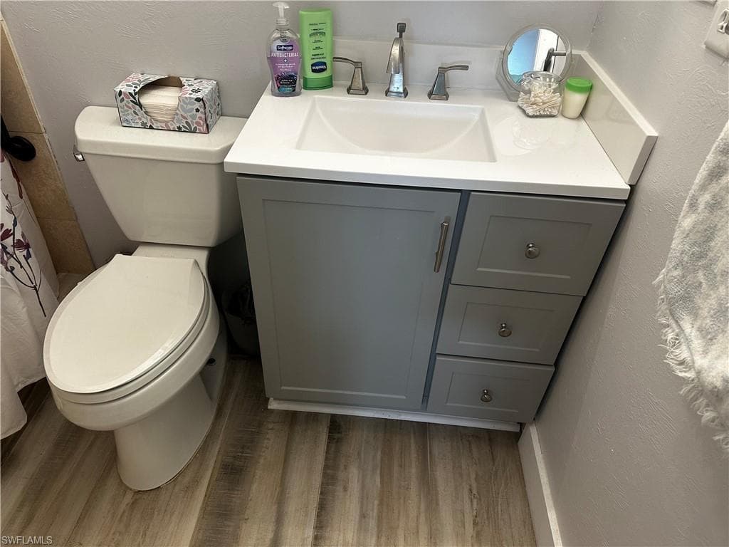 Bathroom with a textured wall, vanity, curtained shower, and light wood finished floors