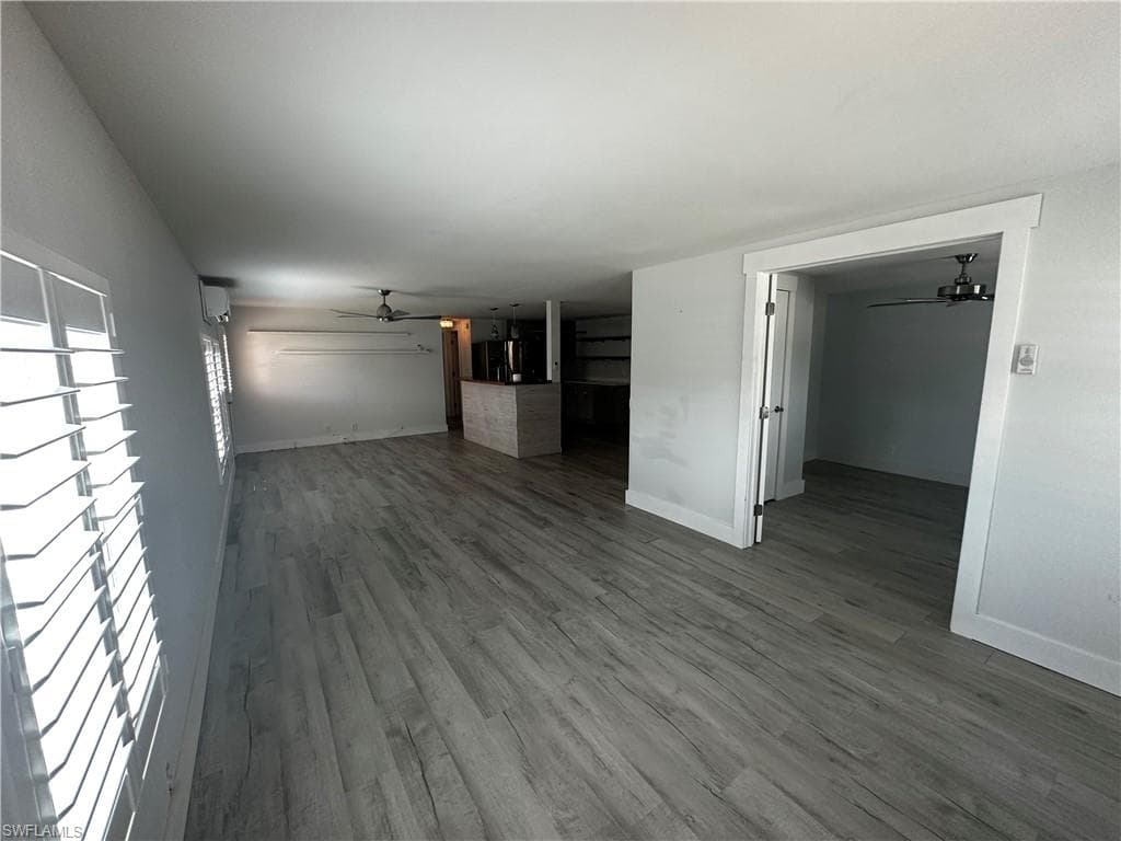 Unfurnished living room with a ceiling fan and dark wood-type flooring