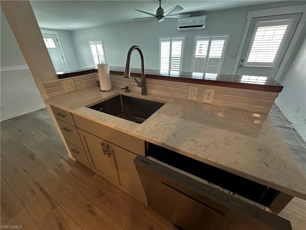 Kitchen with dishwasher, light wood-style floors, light stone countertops, and a ceiling fan