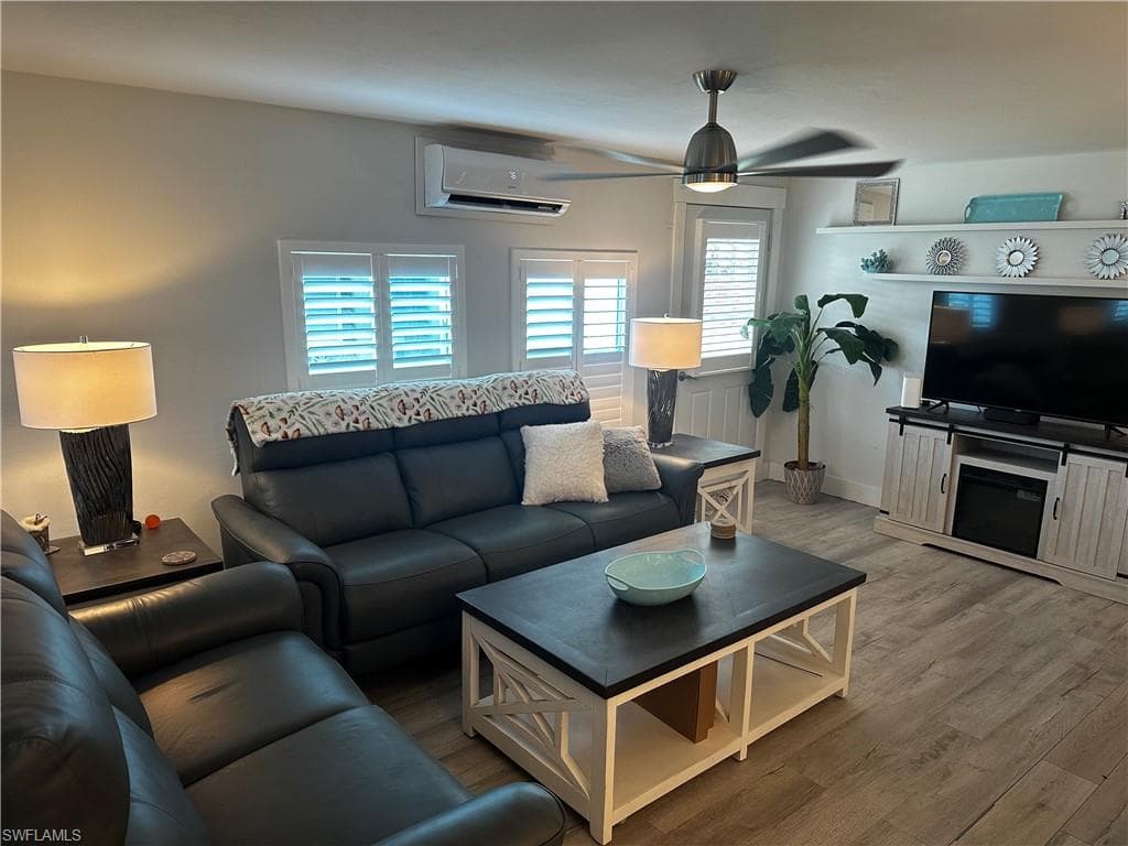 Living room with a ceiling fan, a mini split for heating / cooling, and wood finished floors