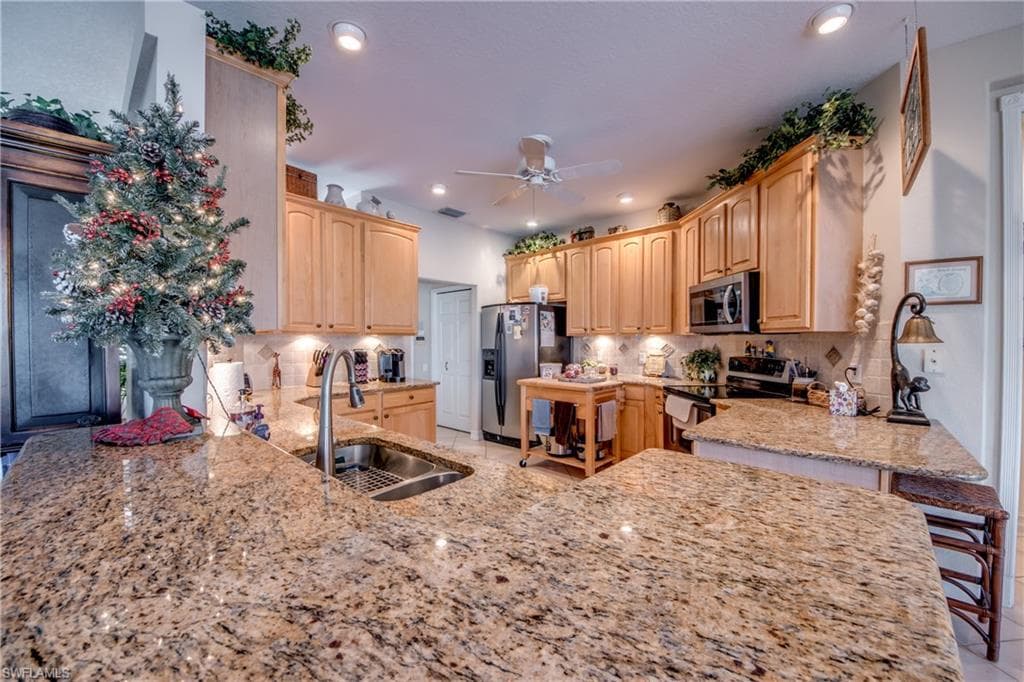 Kitchen with stainless steel appliances, light stone countertops, light wood finish cabinets, ceiling fan, and recessed lighting