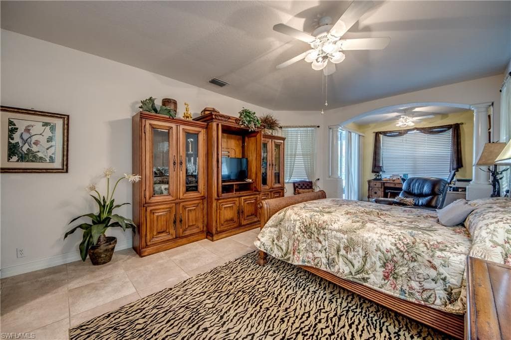 Bedroom with light tile patterned floors, arched walkways, and ceiling fan