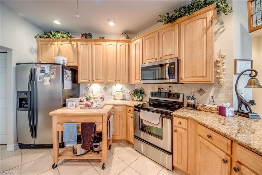 Kitchen with light wood finish cabinetry, stainless steel appliances, light stone countertops, and decorative backsplash