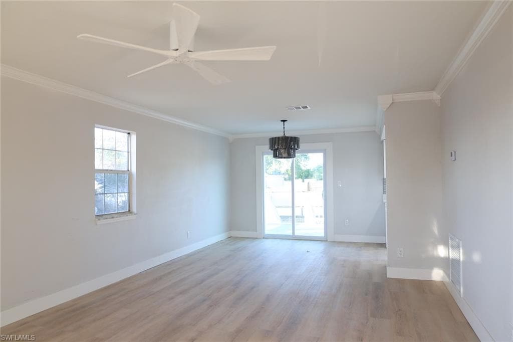 Unfurnished room with light wood-style flooring, crown molding, ceiling fan, suspended lighting, and plenty of natural light