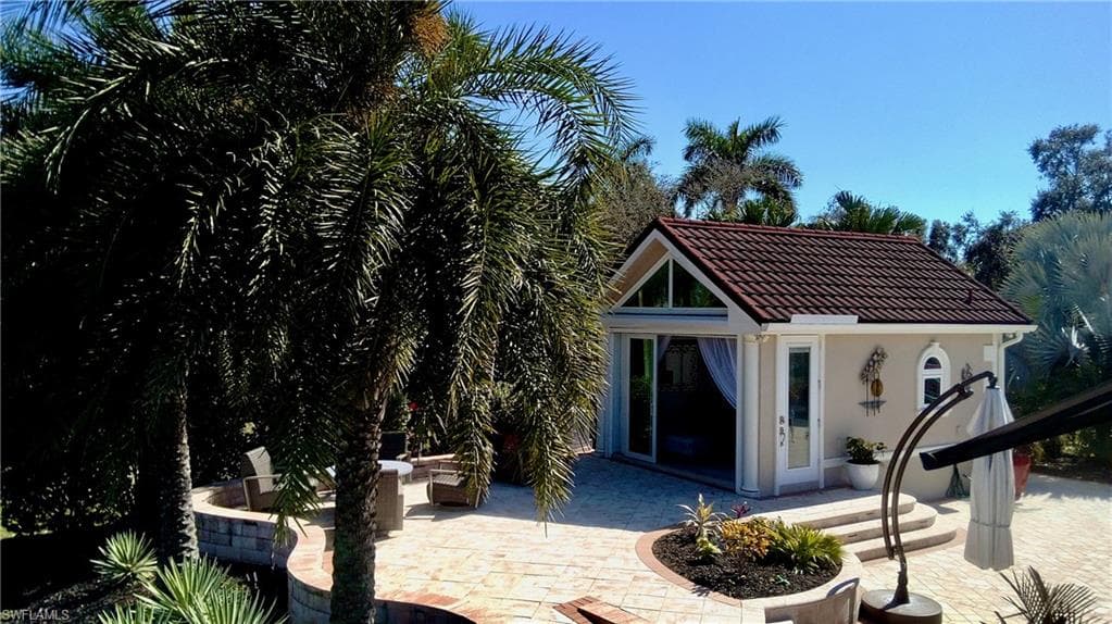 Rear view of property featuring an outdoor structure, a patio area, stucco siding, a tiled roof, and an exterior structure