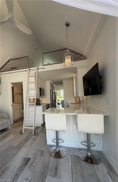 Kitchen with a breakfast bar area, white cabinets, a peninsula, light wood-style floors, and stainless steel appliances