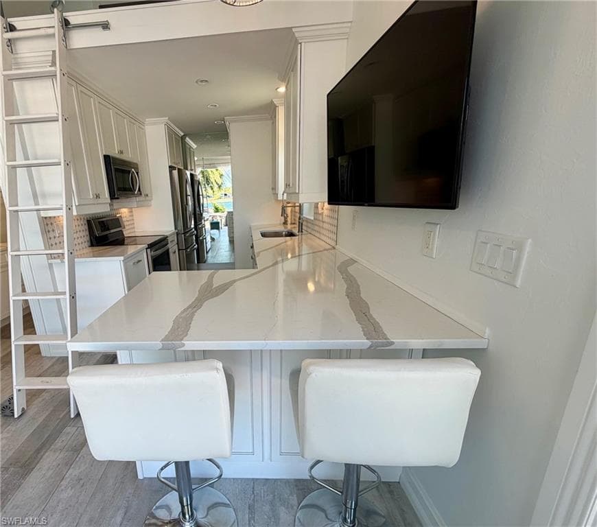Kitchen featuring a breakfast bar area, white cabinets, stainless steel appliances, and a peninsula