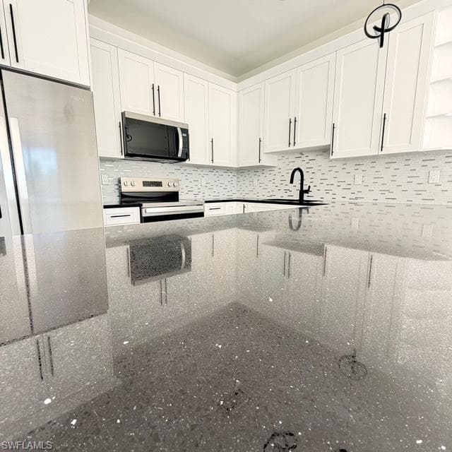 Kitchen with white cabinetry, stainless steel appliances, dark stone countertops, decorative backsplash, and open shelves