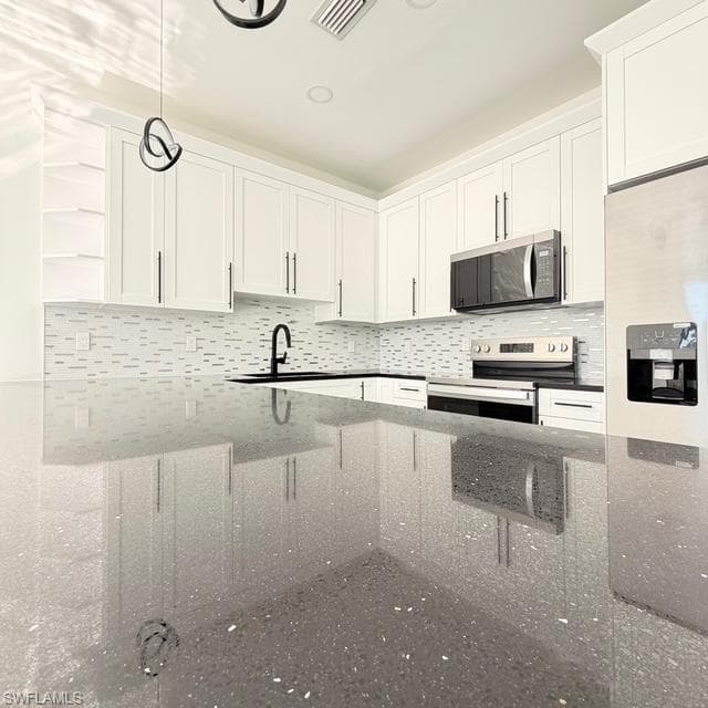 Kitchen with decorative light fixtures, white cabinets, stainless steel appliances, and dark stone countertops