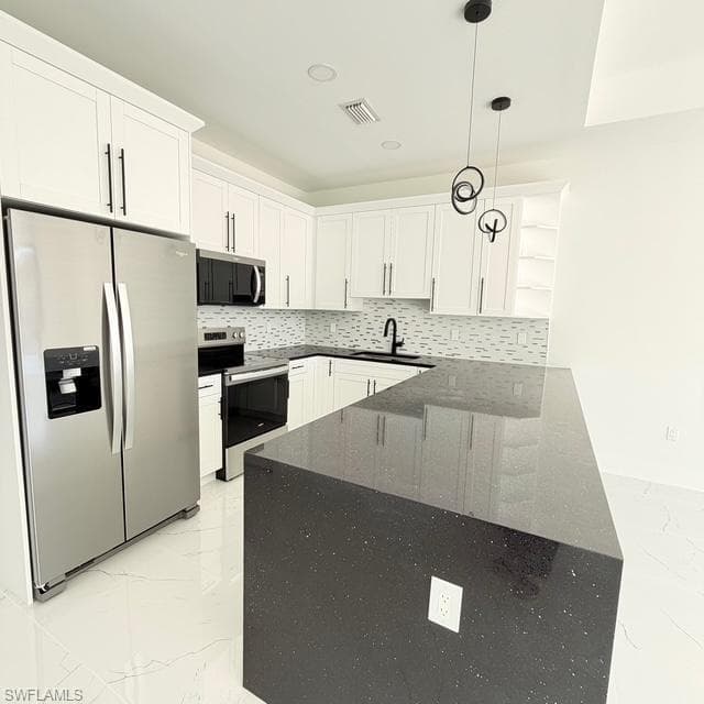 Kitchen with stainless steel appliances, dark stone countertops, hanging light fixtures, white cabinets, and backsplash