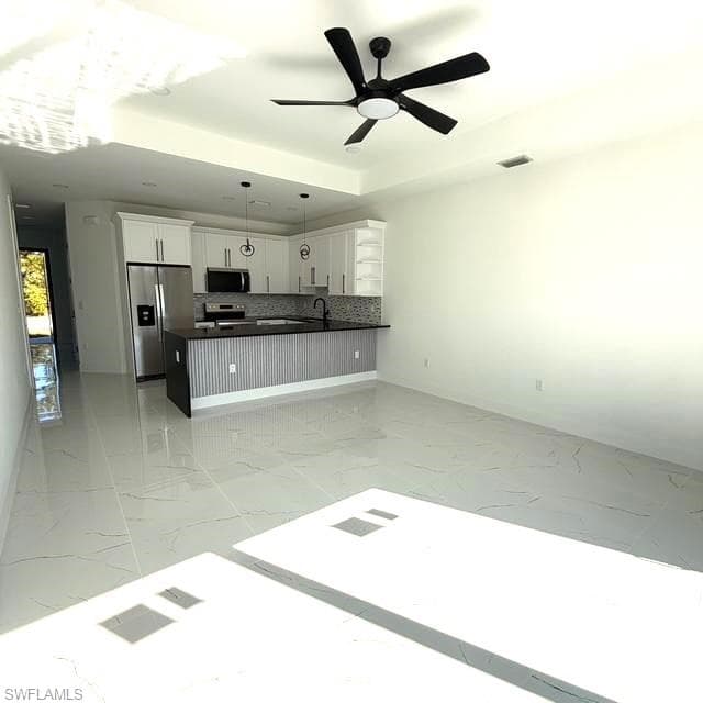 Kitchen featuring white cabinetry, open floor plan, stainless steel appliances, decorative light fixtures, and light marble finish flooring