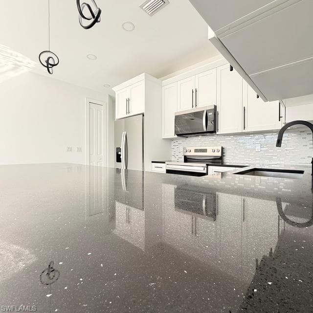 Kitchen featuring white cabinets, dark stone counters, stainless steel appliances, and hanging light fixtures