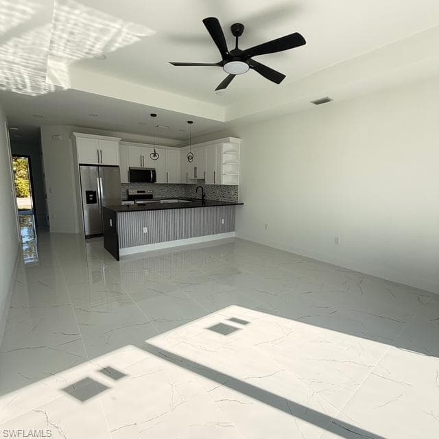 Kitchen with open floor plan, stainless steel appliances, white cabinets, ceiling fan, and a peninsula