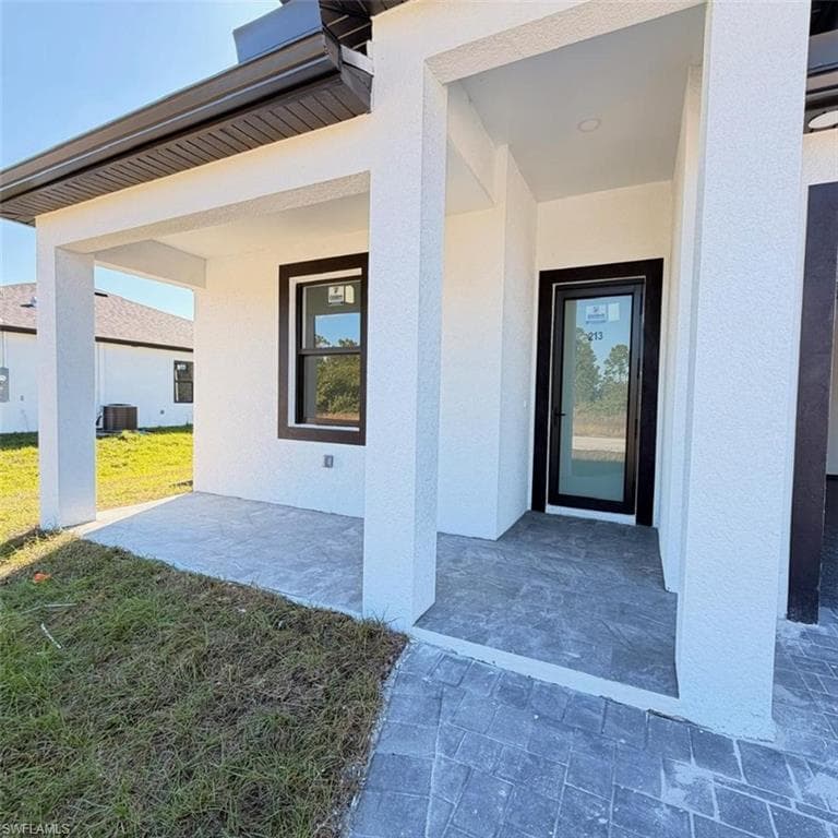 View of exterior entry with a patio, a yard, and stucco siding