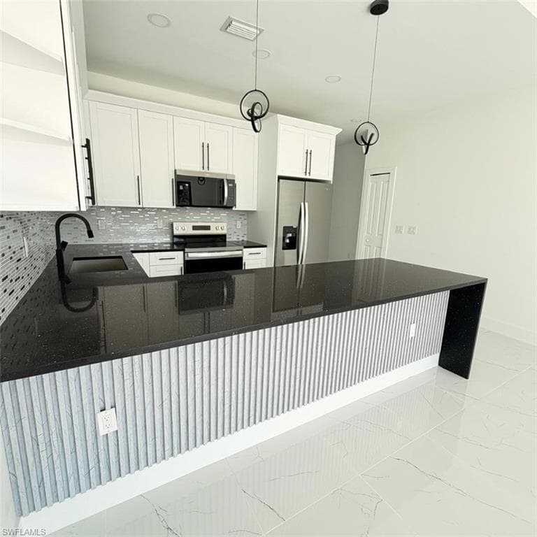 Kitchen featuring dark stone countertops, stainless steel appliances, a peninsula, and white cabinetry