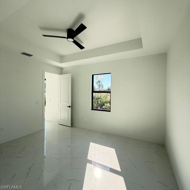 Spare room with light marble finish flooring, a tray ceiling, and a ceiling fan