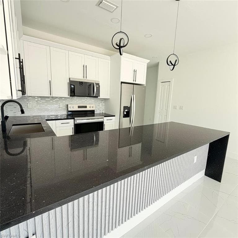 Kitchen with dark stone countertops, stainless steel appliances, white cabinets, tasteful backsplash, and a peninsula