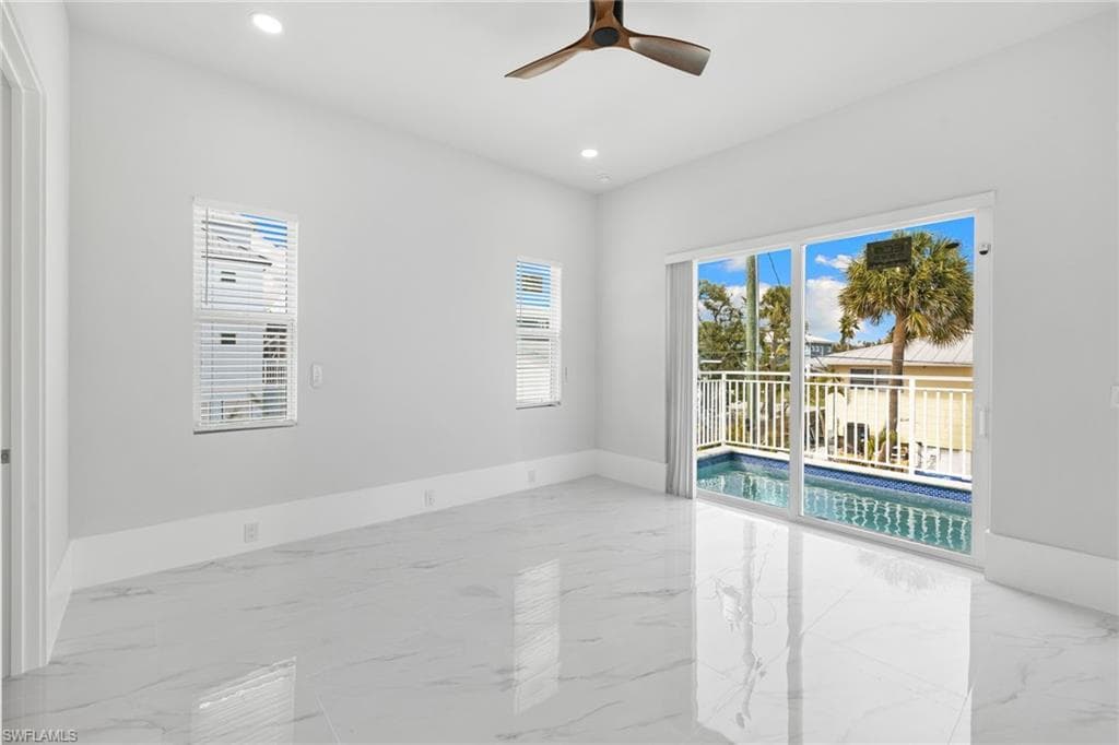 Spare room featuring a ceiling fan, healthy amount of natural light, light marble finish flooring, and recessed lighting