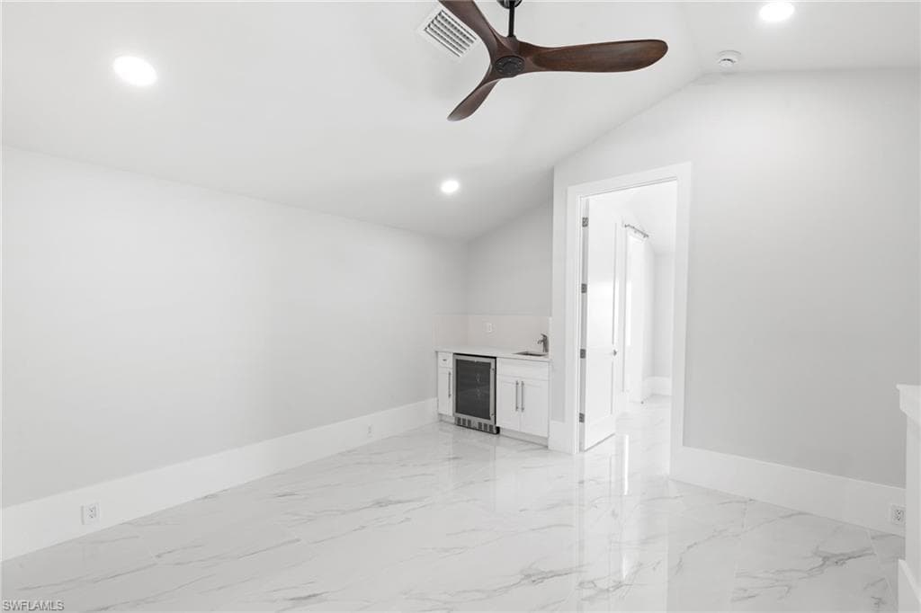 Unfurnished room with beverage cooler, recessed lighting, a ceiling fan, light marble finish flooring, and lofted ceiling
