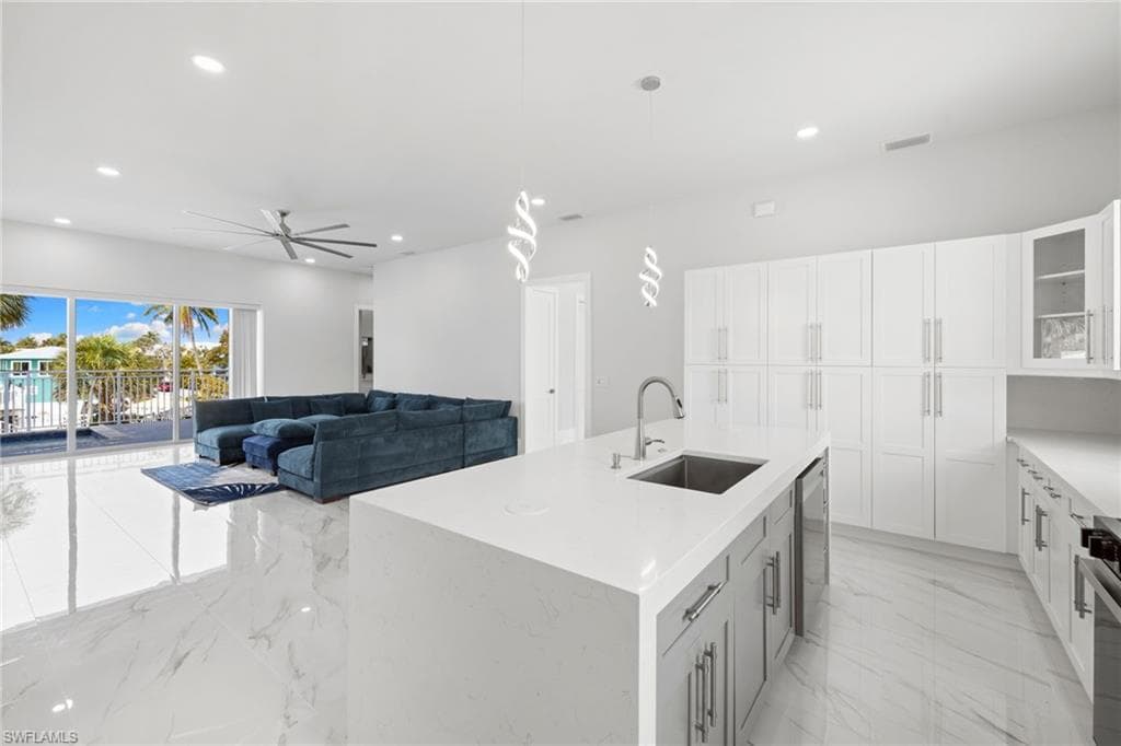 Kitchen featuring a kitchen island with sink, glass fronted cabinets, a ceiling fan, decorative light fixtures, and light stone countertops