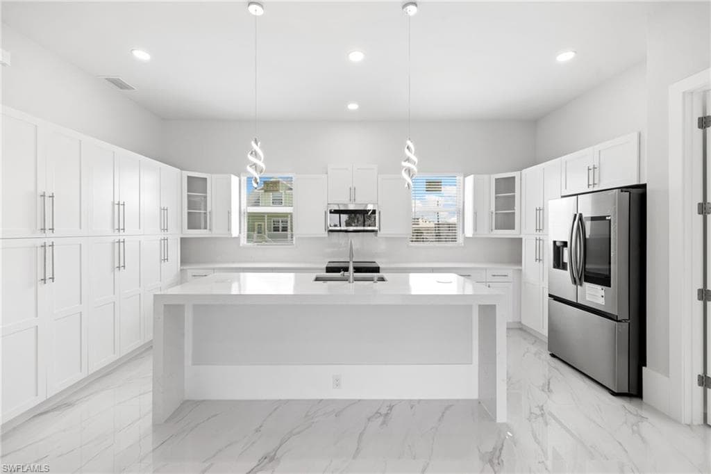 Kitchen with glass insert cabinets, stainless steel appliances, a kitchen island with sink, and light stone counters