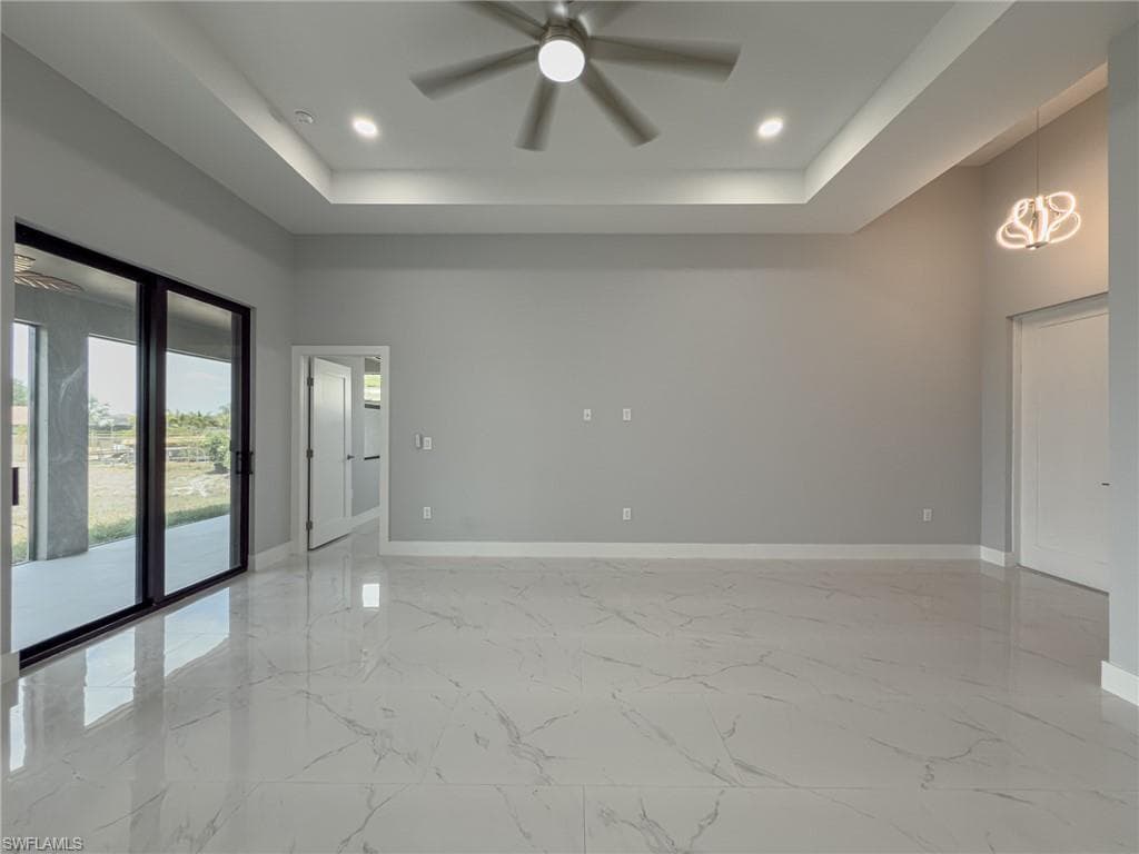 Empty room with recessed lighting, ceiling fan with notable chandelier, a raised ceiling, and baseboards