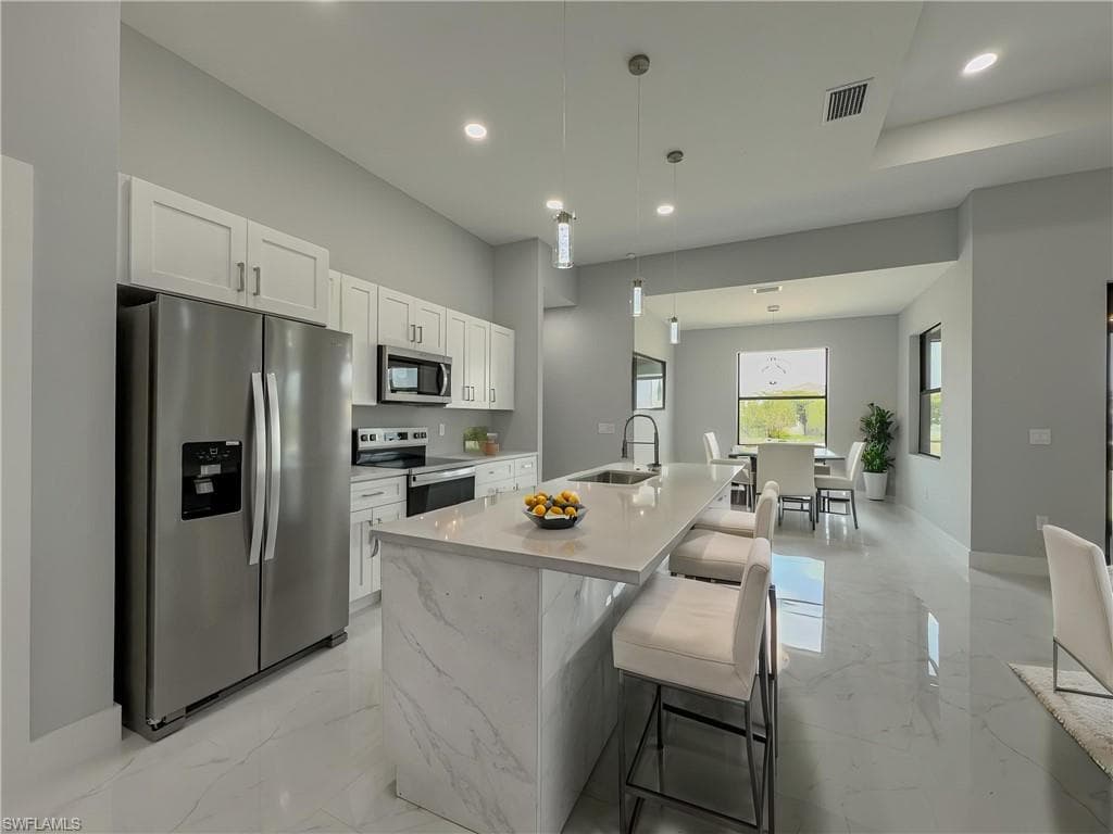 Kitchen with a sink, white cabinets, stainless steel appliances, and marble finish floor