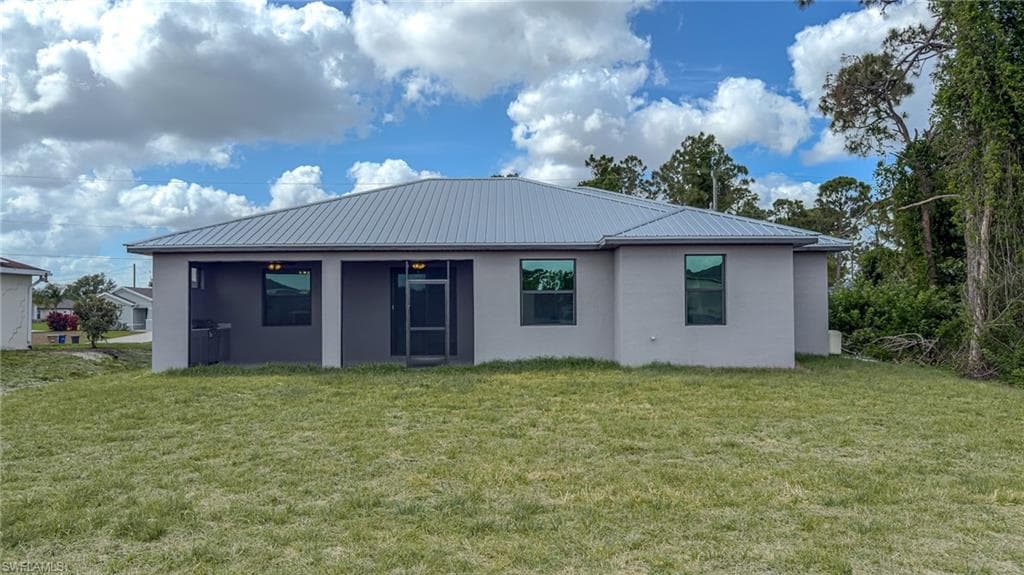 Rear view of house featuring stucco siding, a yard, and metal roof