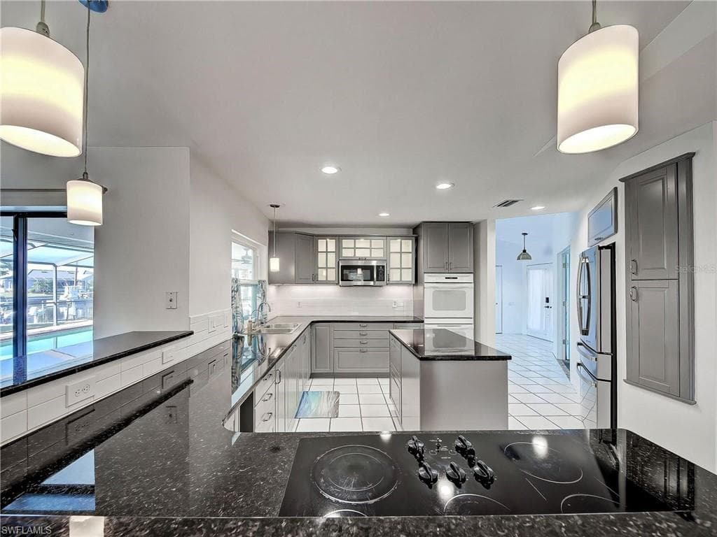Kitchen featuring hanging light fixtures, gray cabinets, stainless steel appliances, glass fronted cabinets, and a kitchen island