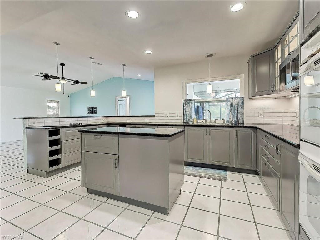Kitchen with gray cabinets, healthy amount of natural light, pendant lighting, and lofted ceiling
