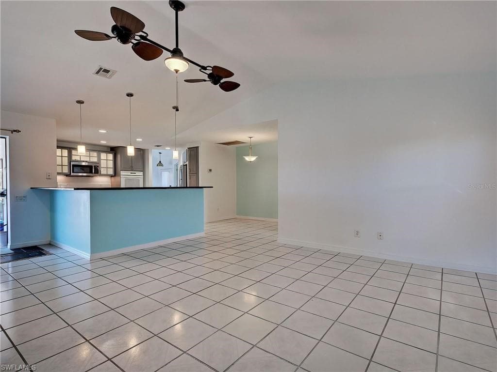 Kitchen with a ceiling fan, dark countertops, a peninsula, pendant lighting, and vaulted ceiling