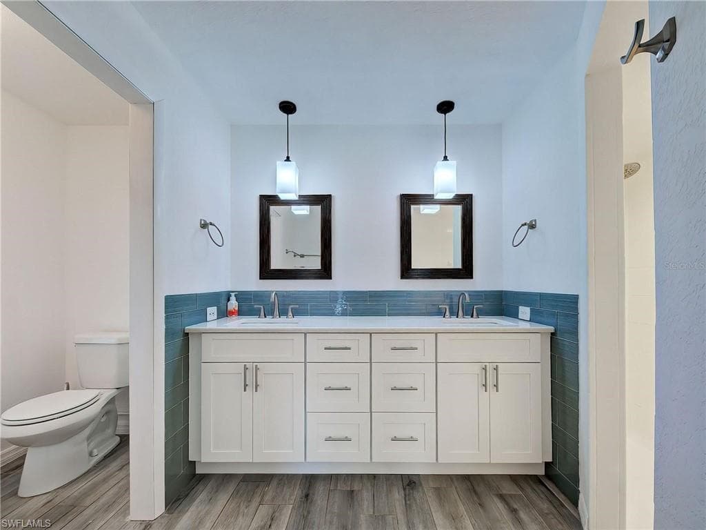 Bathroom with tile walls, double vanity, light wood finished floors, a wainscoted wall, and a shower