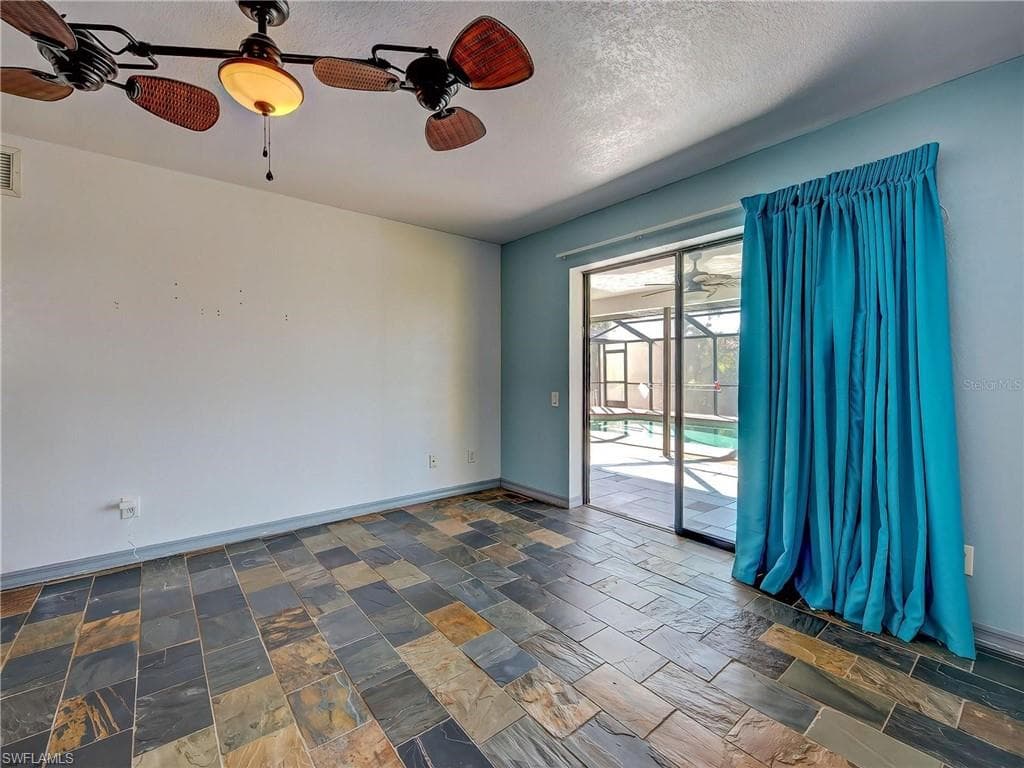 Empty room featuring a ceiling fan, stone tile floors, and a textured ceiling