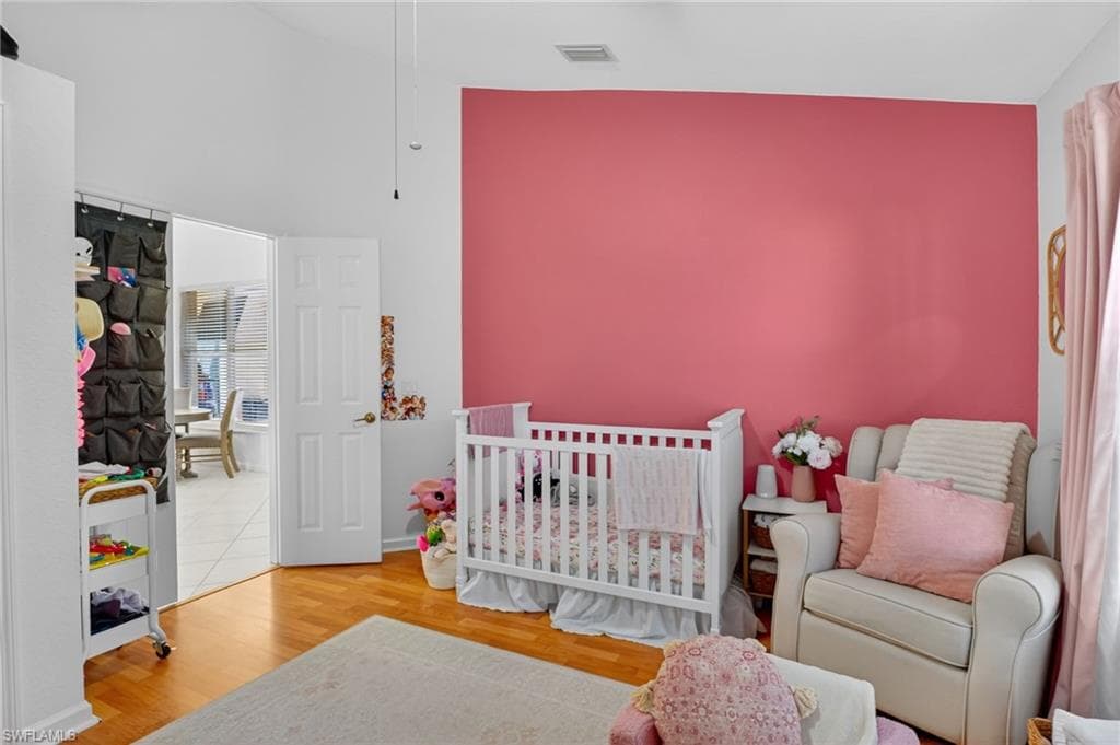 Bedroom featuring light wood-style flooring, a crib, and vaulted ceiling