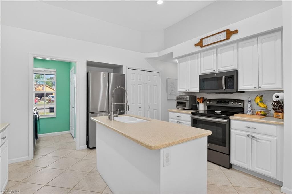 Kitchen featuring stainless steel appliances, white cabinets, a kitchen island with sink, light tile patterned flooring, and recessed lighting