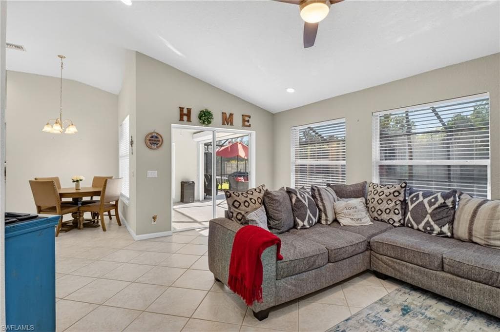 Living area featuring light tile patterned flooring, healthy amount of natural light, vaulted ceiling, ceiling fan, and a chandelier