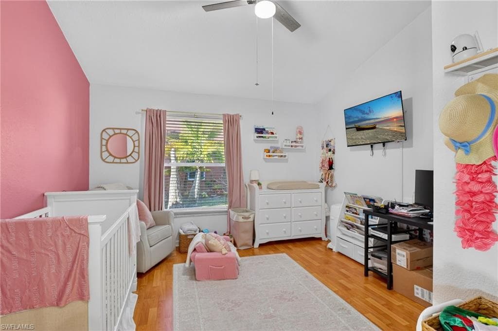Bedroom with a nursery area, light wood-style flooring, vaulted ceiling, and a ceiling fan