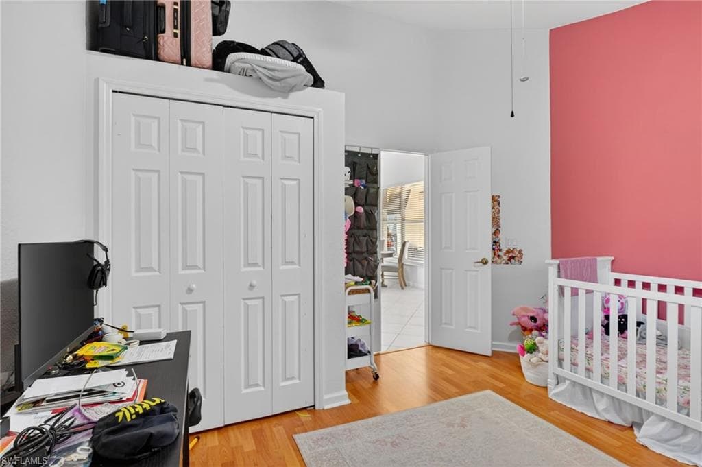 Bedroom featuring light wood-style floors, a nursery area, a closet, and a high ceiling