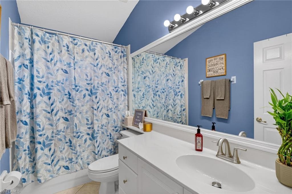 Bathroom with vanity, shower / bath combo with shower curtain, light tile patterned flooring, and vaulted ceiling