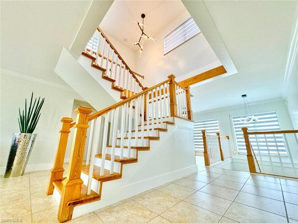 Stairway with suspended lighting, crown molding, and tile patterned floors