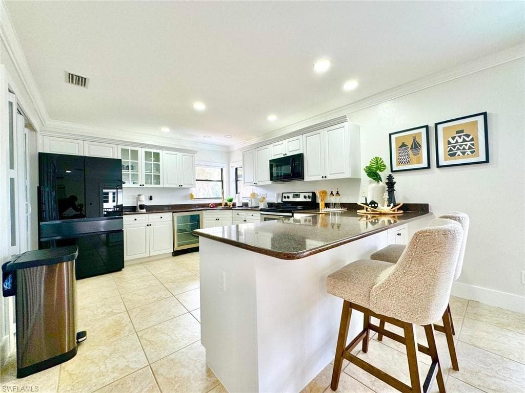 Kitchen featuring a peninsula, black appliances, a kitchen breakfast bar, white cabinets, and crown molding