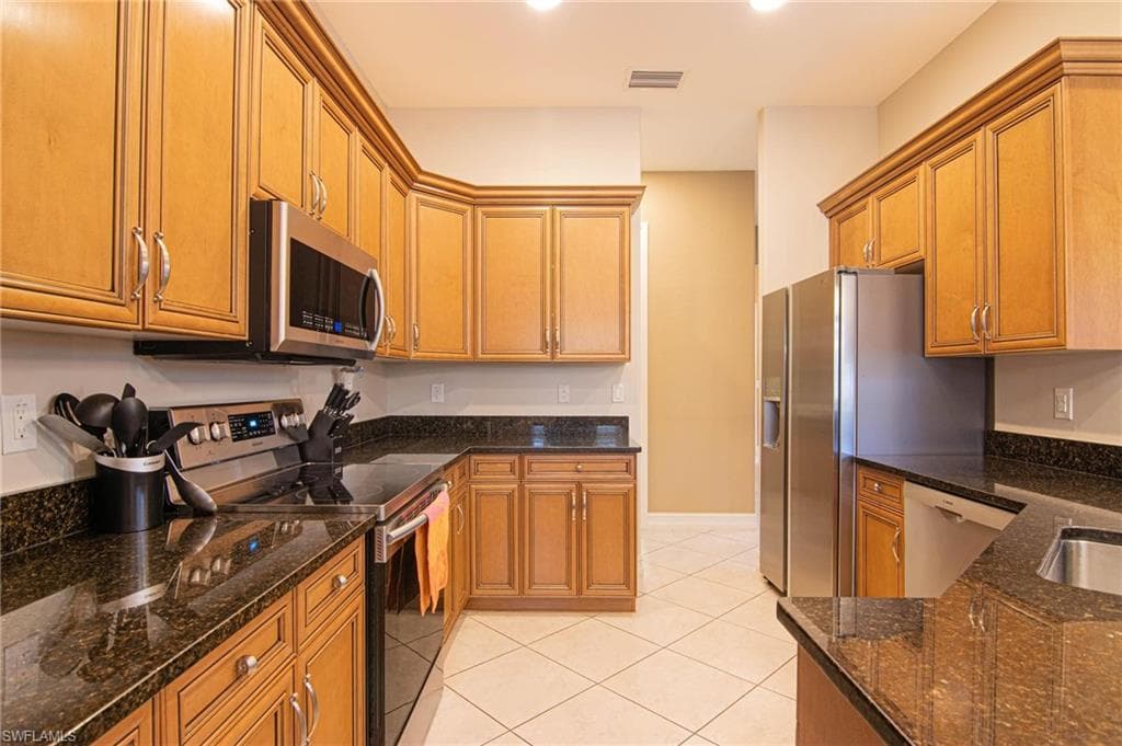 Kitchen with stainless steel appliances, wood finish cabinets, dark stone counters, and light tile patterned flooring