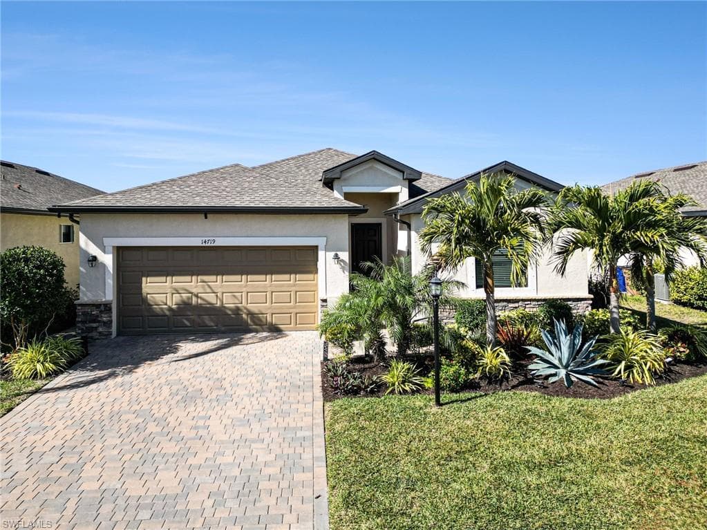 View of front of home with stucco siding, decorative driveway, a front yard, and an attached garage