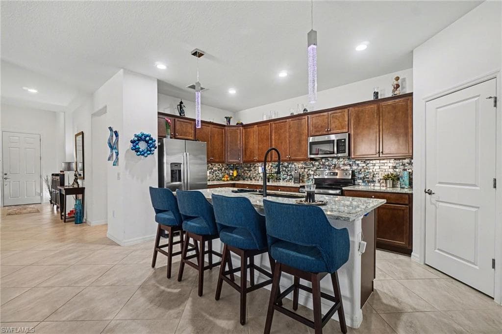 Kitchen with a kitchen breakfast bar, a kitchen island with sink, hanging light fixtures, light stone countertops, and stainless steel appliances