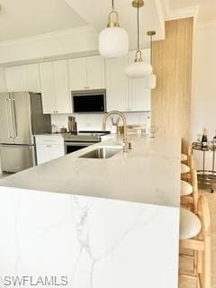 Kitchen with stainless steel appliances, white cabinets, pendant lighting, light stone counters, and kitchen peninsula