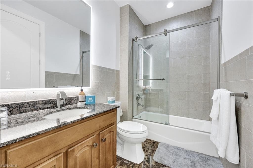 Full bathroom with tile walls, shower / bath combination with glass door, vanity, and wainscoting