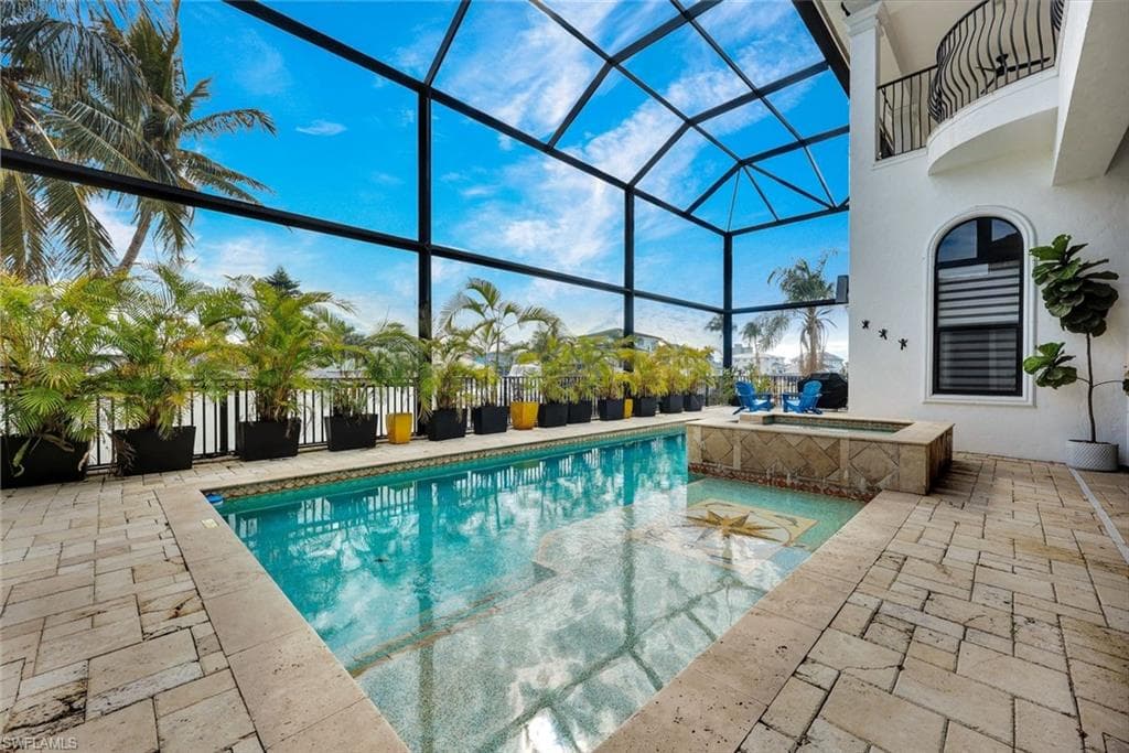 Swimming pool with glass enclosure, a patio area, a sunroom, and an in-ground hot tub