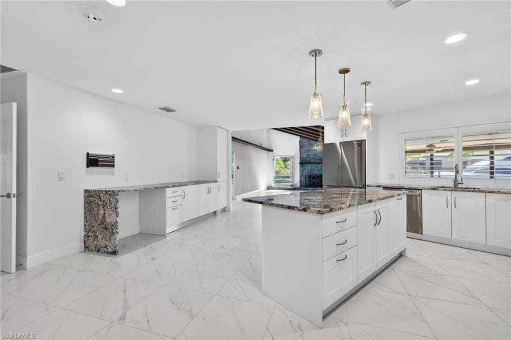Kitchen with dark stone countertops, light marble finish floors, and a kitchen island