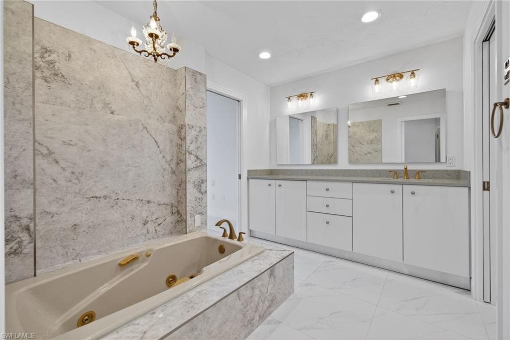 Full bath with a jetted tub, double vanity, light marble finish flooring, and suspended lighting